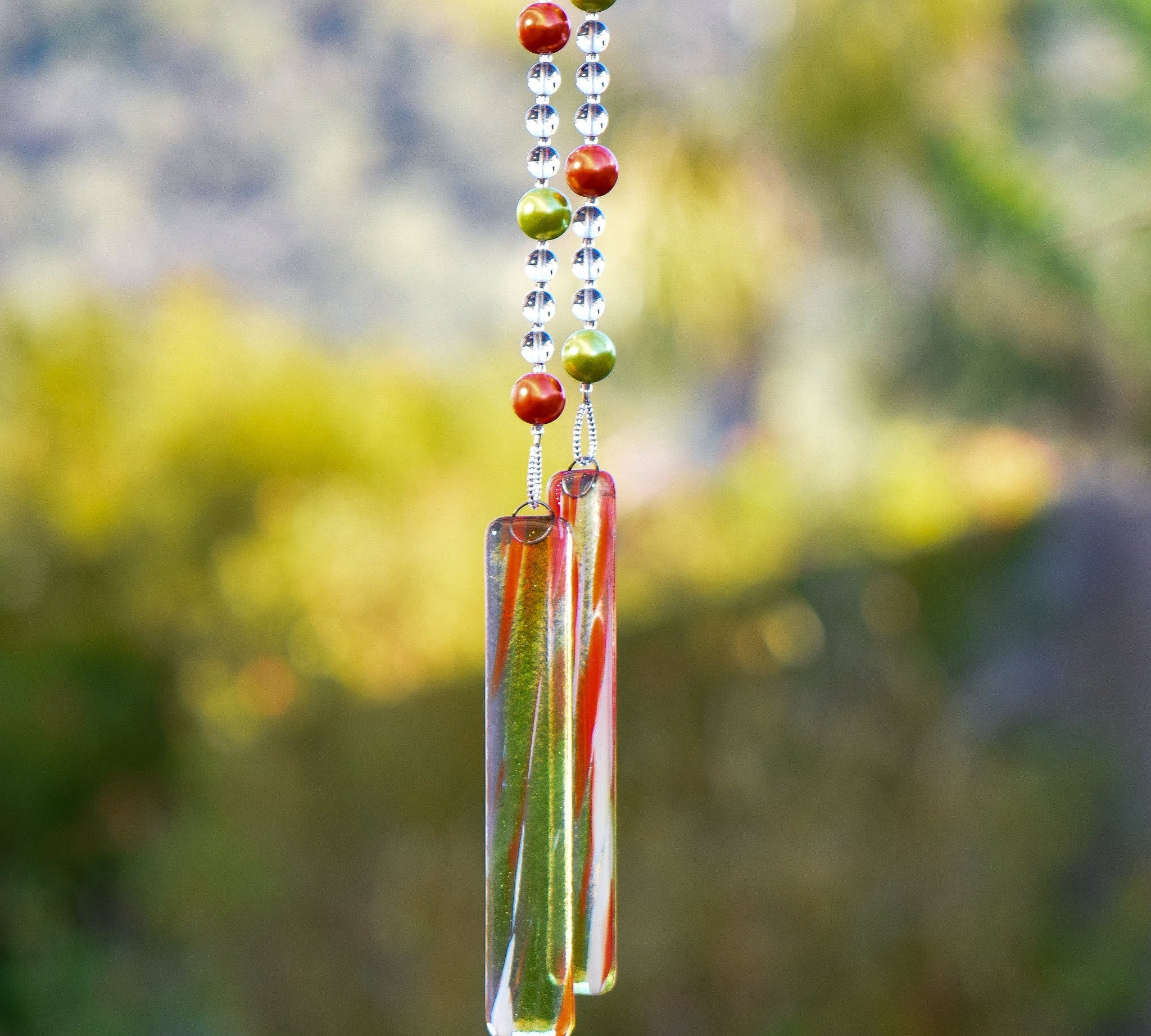 LIme green and bright orange pearl beads strung with smaller clear beads, hanging vertically from a tree, anchored by two pieces of clear/orange/green glass.