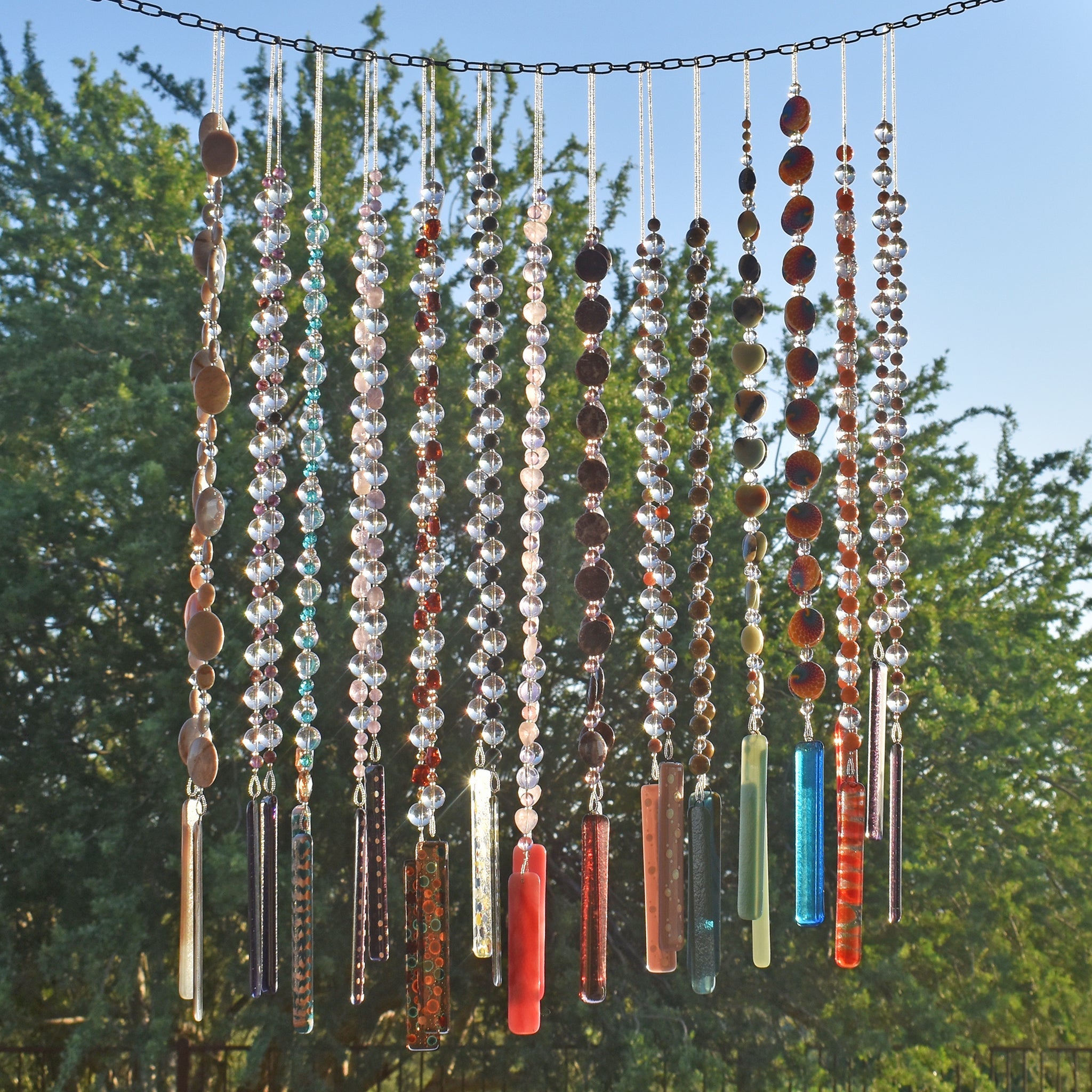 several cinjo handmade wind chimes hanging from chain with ironwood tree and blue sky in background