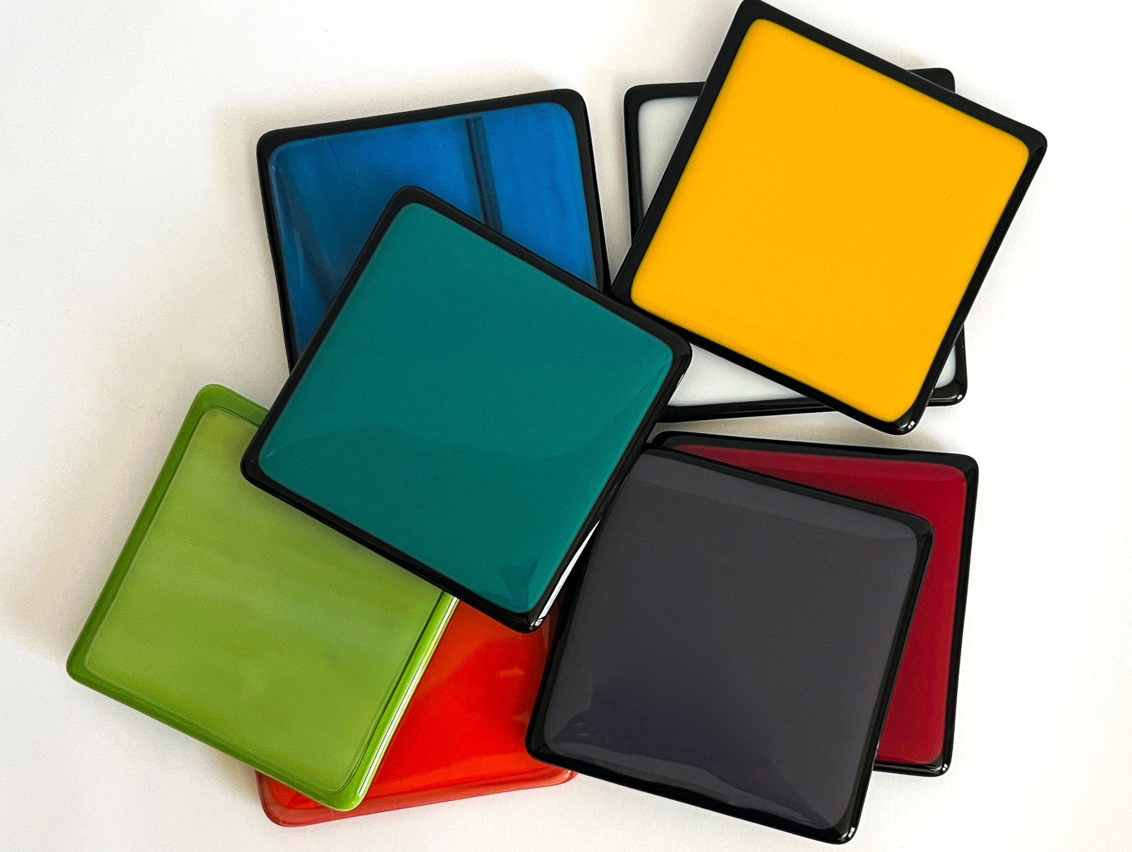 Four inch fused glass coasters in various colors - lime green, teal green, dusty purple, blue, white, red and orange - with white background. 