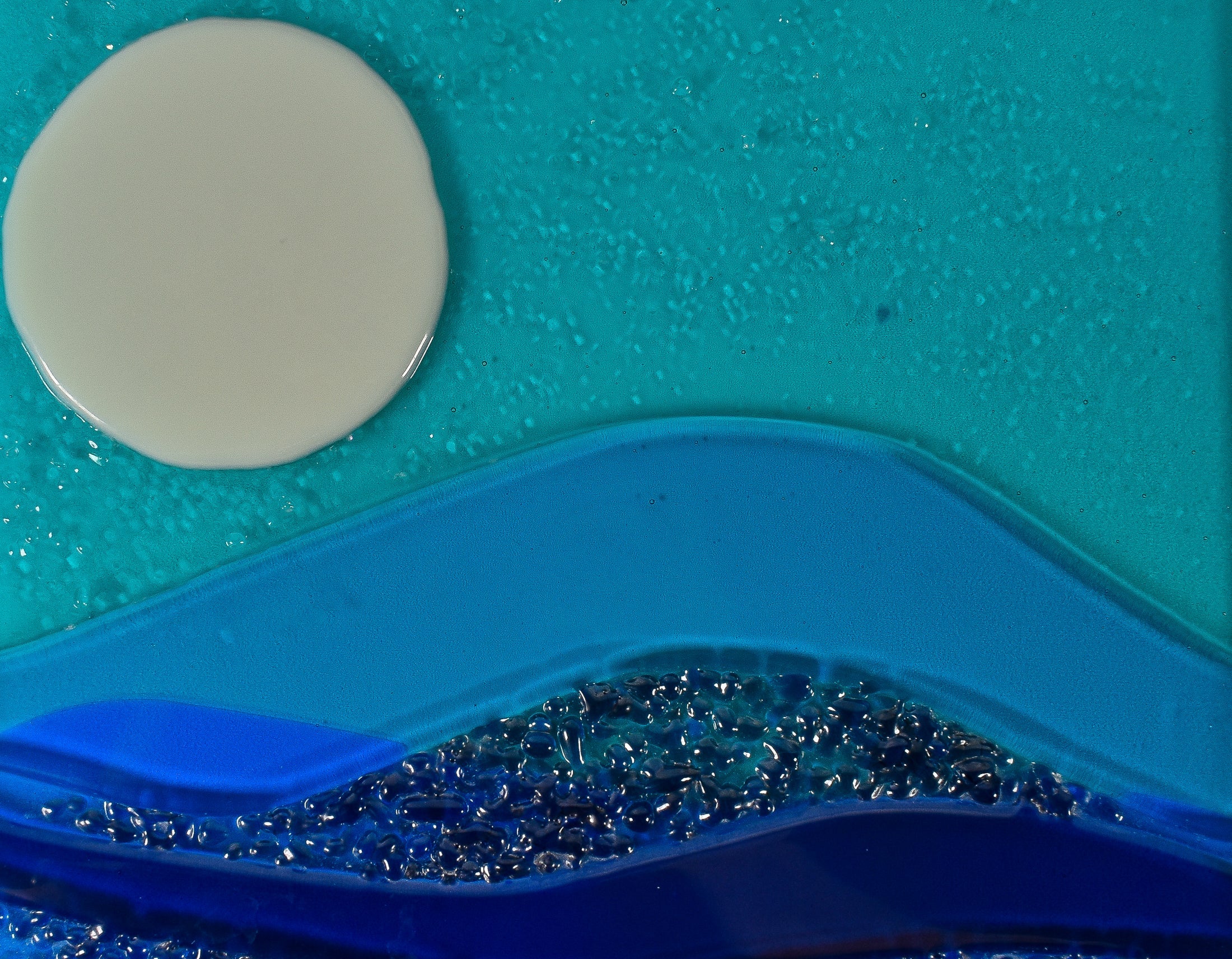 A portion of a piece of fused glass art showing flow and texture in blues, greens and white.