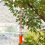 bright orange striped acrylic beads paired with smaller orange beads and  large clear glass beads, strung on wire and hanging vertically, anchored by orange fused glass pieces. hanging from tree