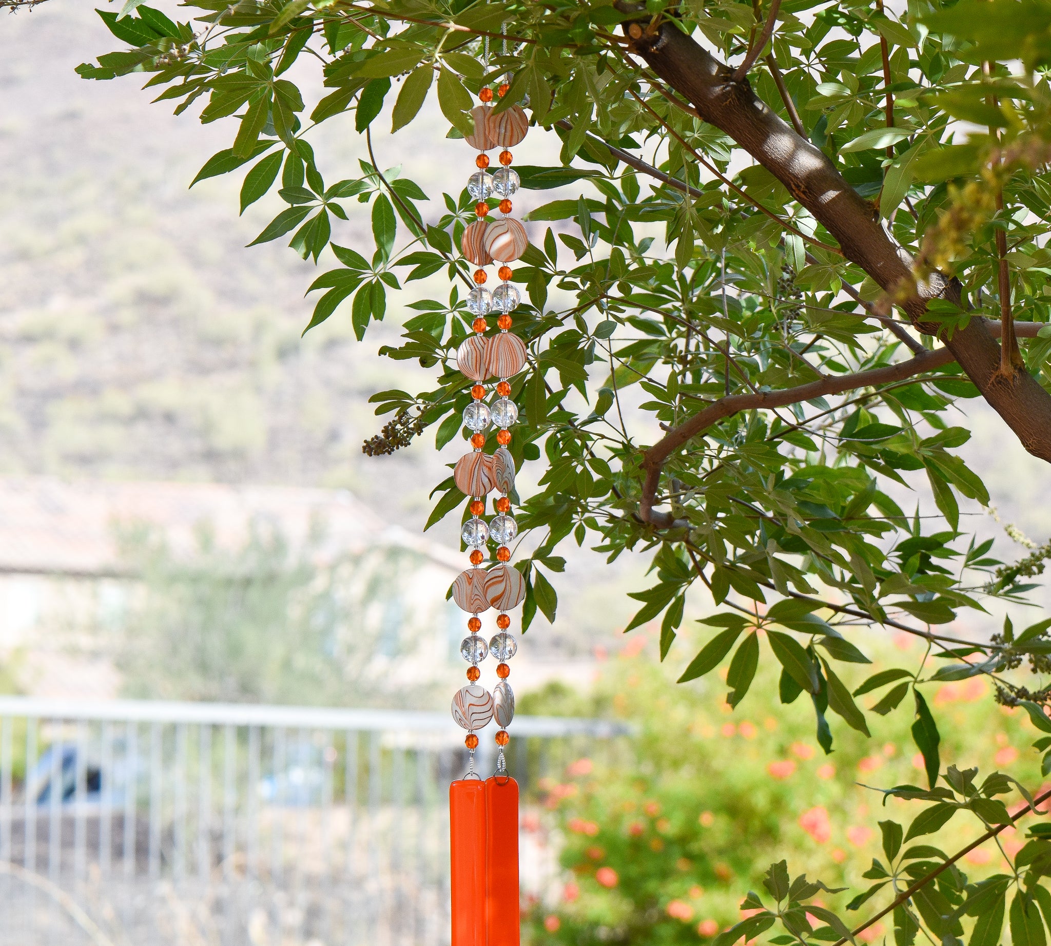 bright orange striped acrylic beads paired with smaller orange beads and  large clear glass beads, strung on wire and hanging vertically, anchored by orange fused glass pieces. hanging from tree