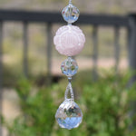 Large round carved rose quartz stone bead flanked by two faceted crystal beads and anchored by a small crystal prism, hanging vertically.