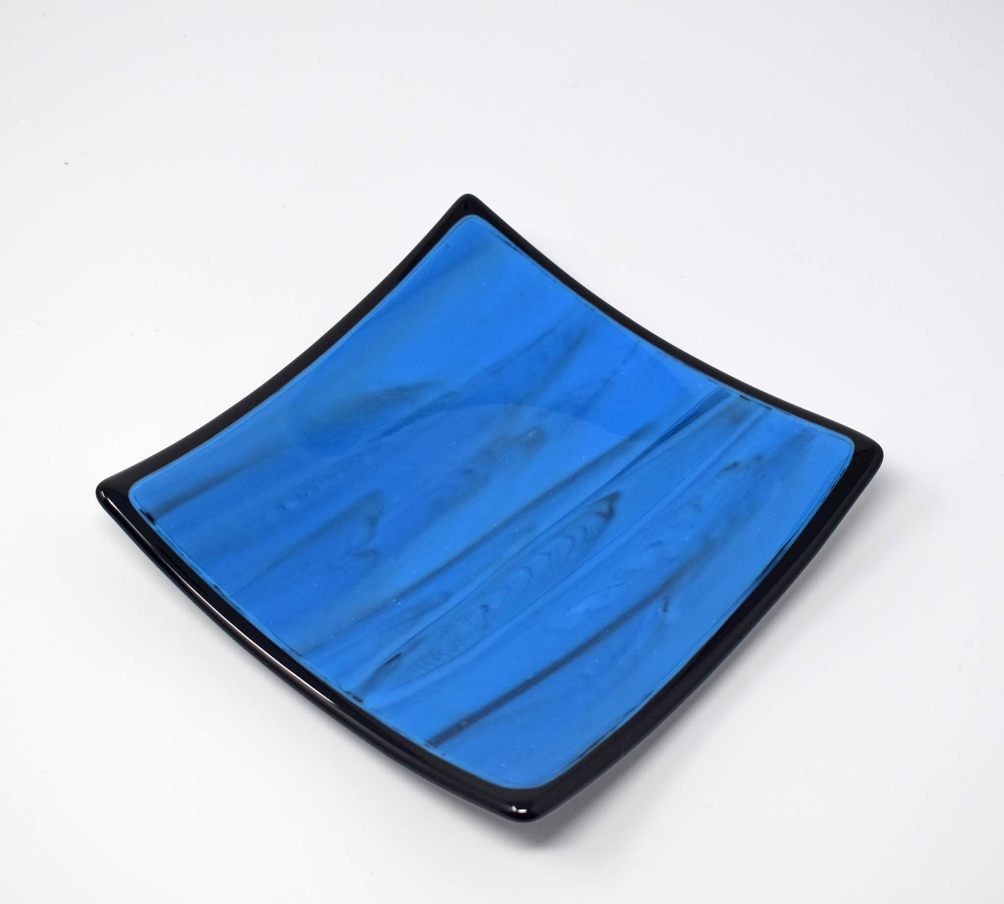 Square blue glass dish with black trim and black designs in the glass, on white background.