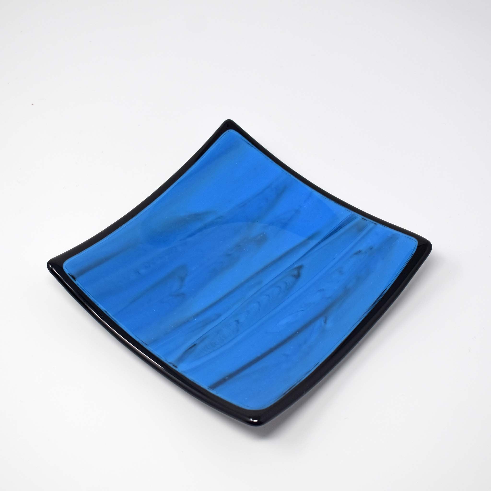 Square blue glass dish with black trim and black designs in the glass, on white background.