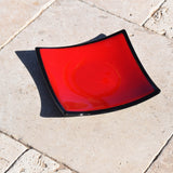 A red glass plate with a black rim. The plate is slightly curved and has a glossy finish.