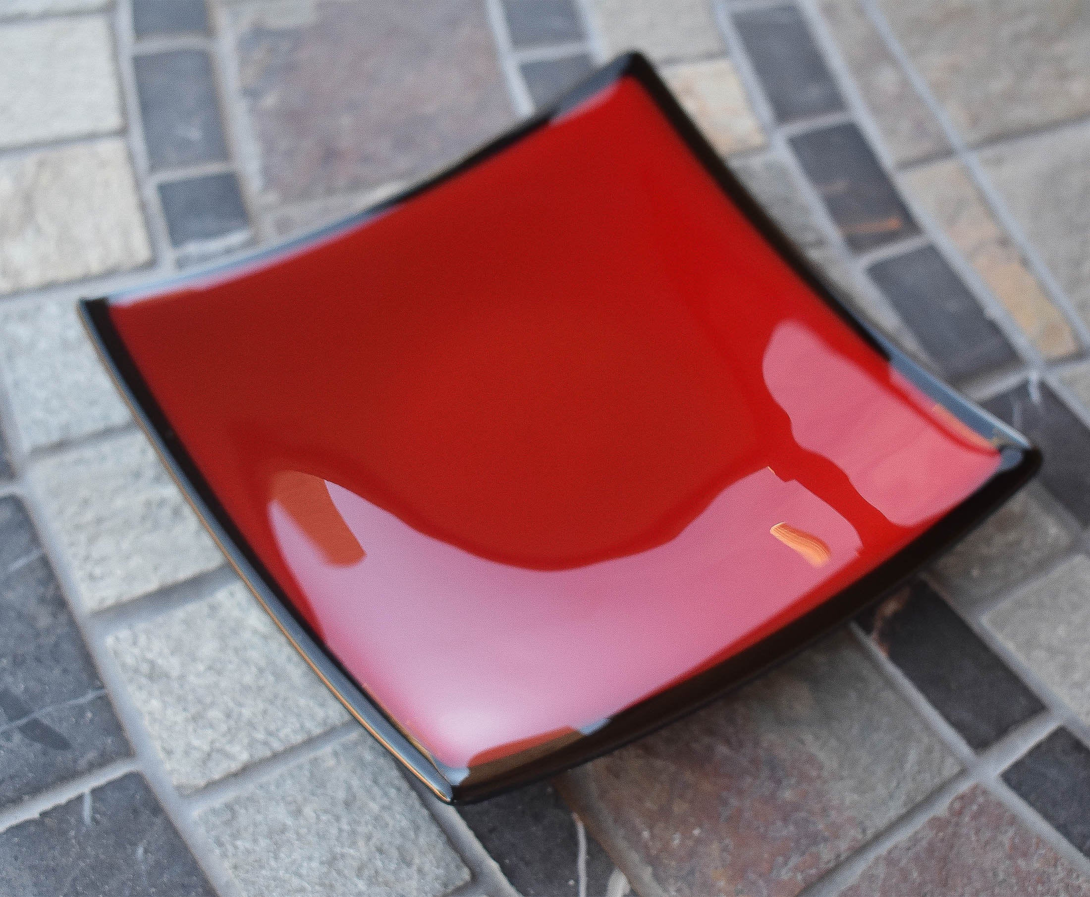 Red, square dish with black trim on stone table