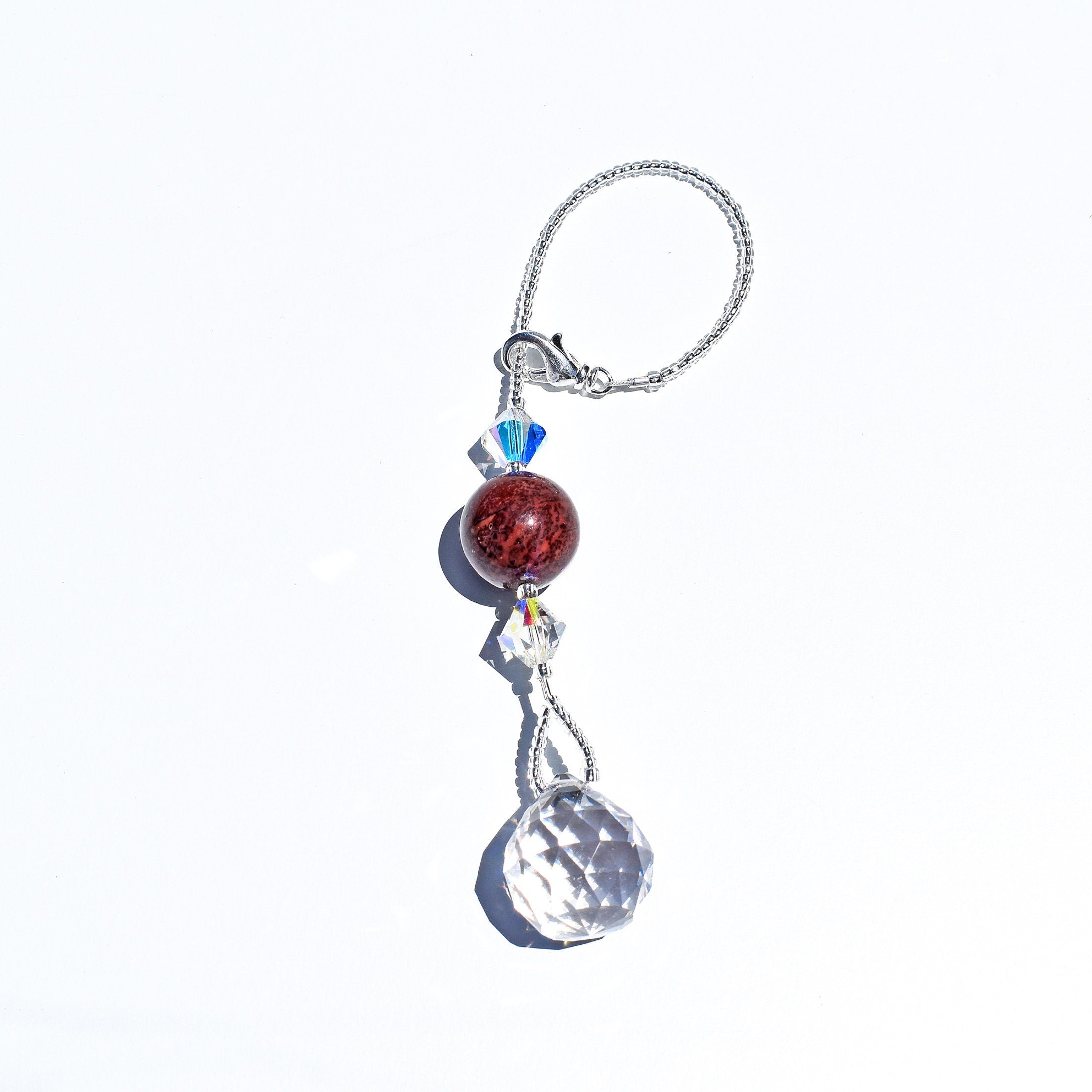 Small sun-catcher strung on wire, laying flat on white background. Includes large zebra jasper stone, flanked by crystal bicone beads, anchored by round crystal prism.