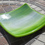 Small, square glass dish in lime green and white on stone table