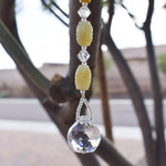 Barrel-shaped jade stone beads flanked by smaller cut crystal beads and anchored by a small, round crystal prism, all hanging vertically from tree.