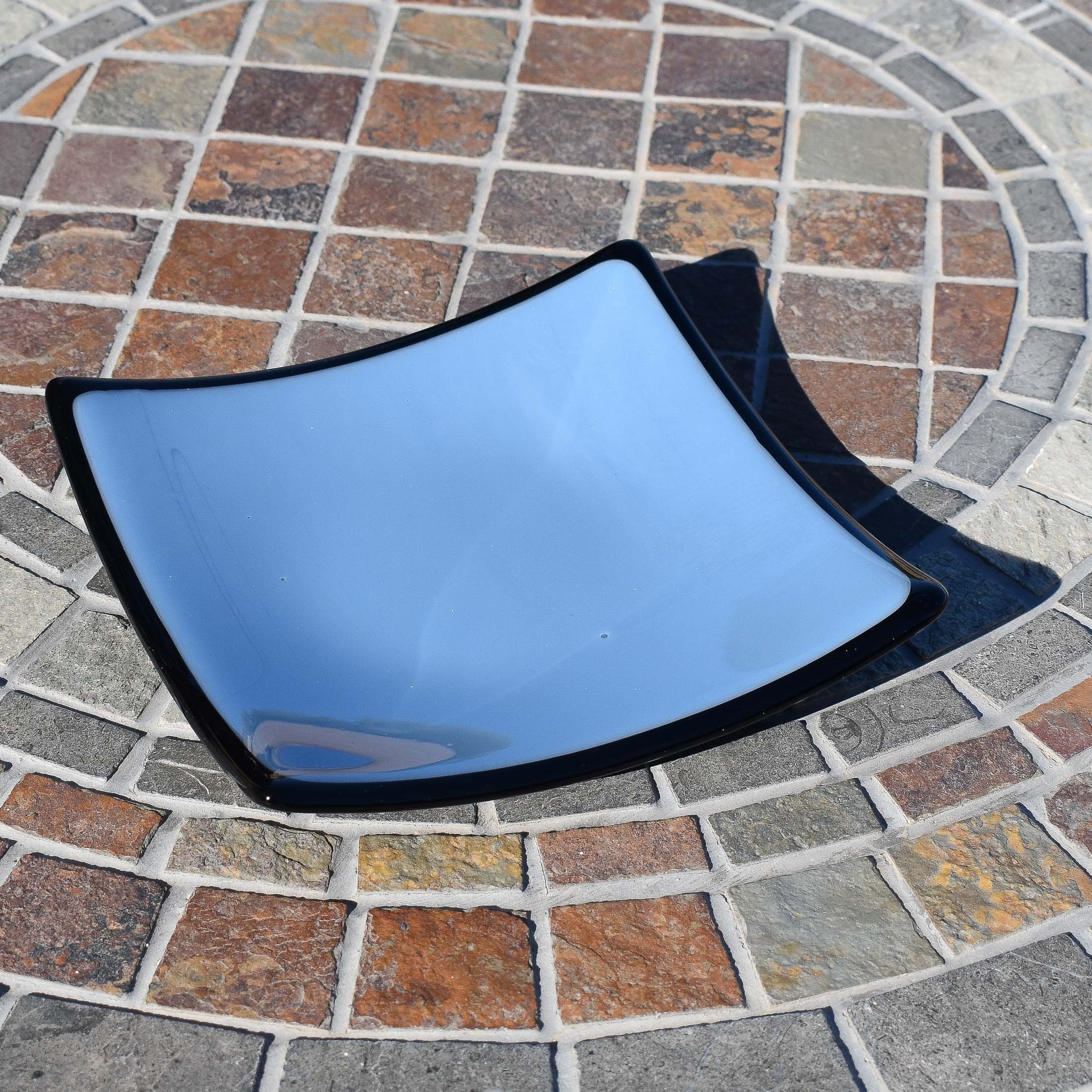 A blue glass plate with black trim and slightly uplifted corners. The plate is sitting on a tiled surface.
