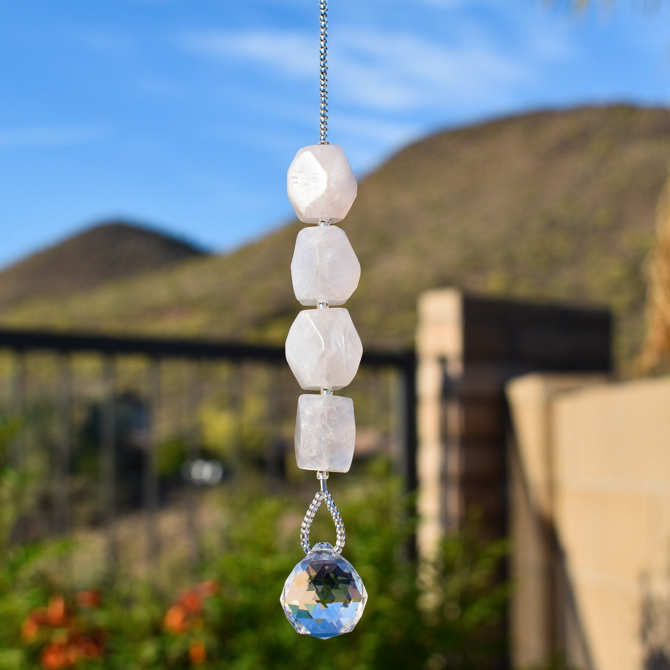 A crystal suncatcher with a clear crystal prism and four pink rose quartz beads hanging from a silver chain.