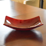 Boat-shaped fused glass dish made of rose red glass, resting on wood table.