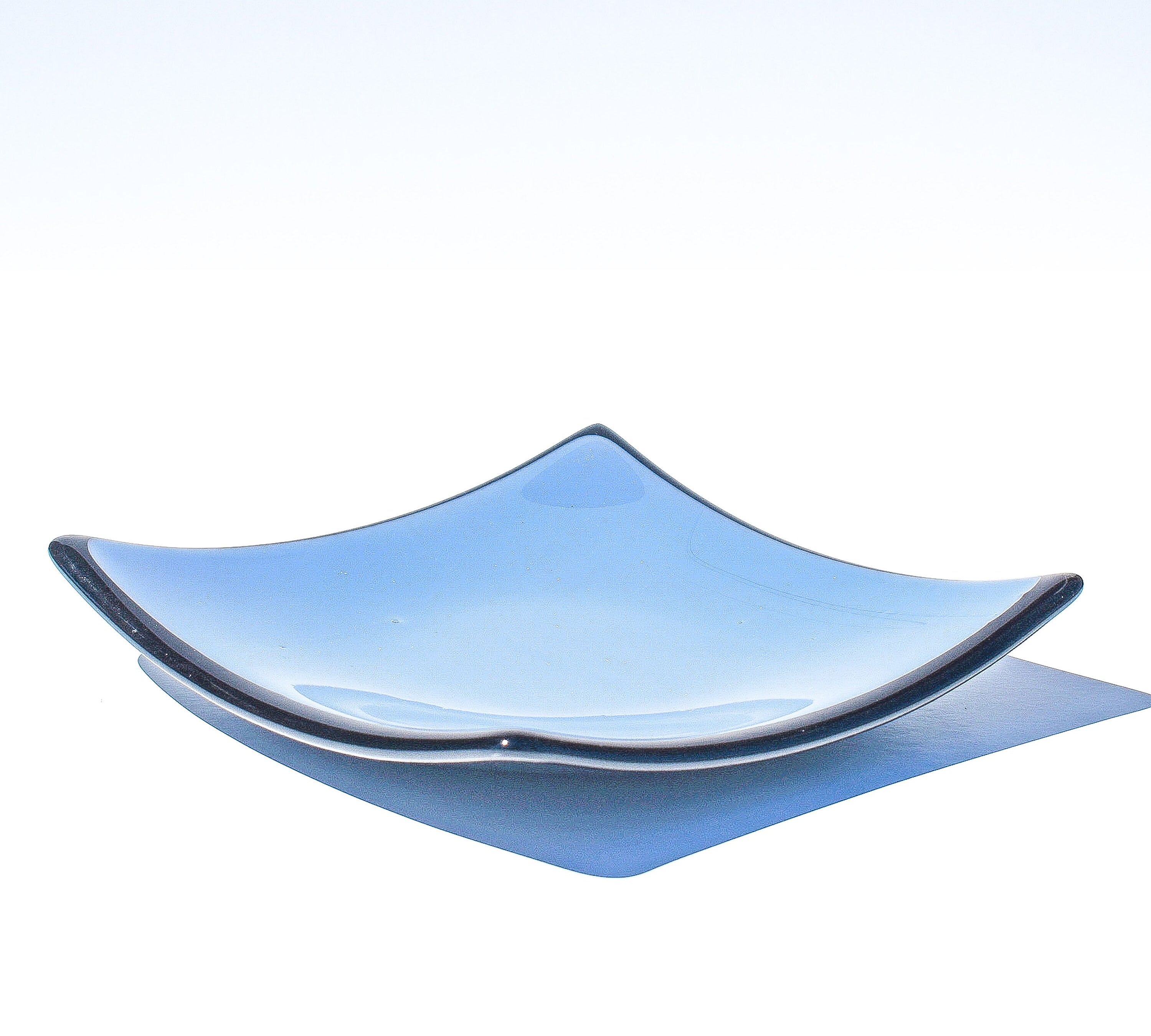 Denim blue square glass dish with black trim and slightly sloped corners, viewed from the side in front of a white background.
