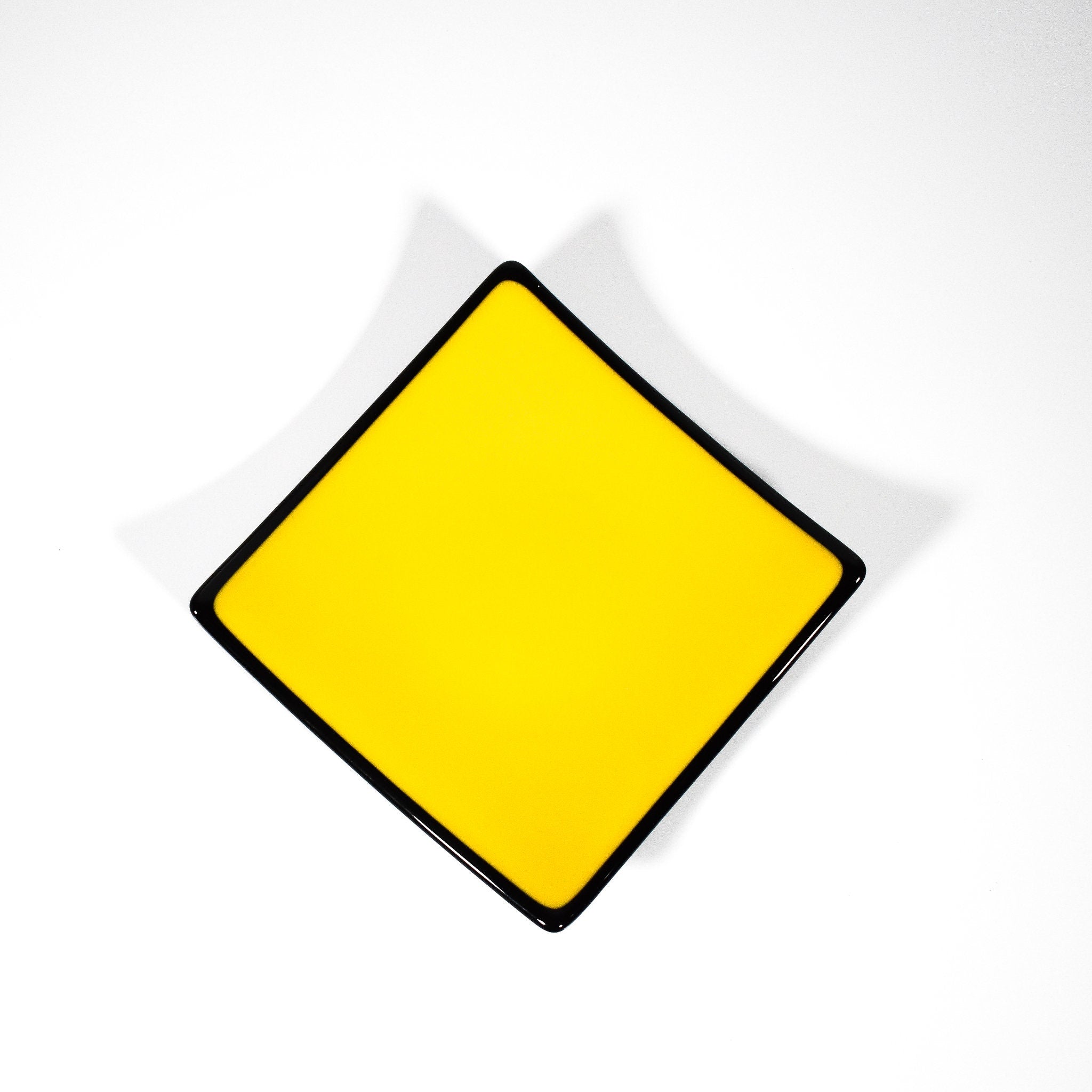 Square kiln-formed glass tray in Sunflower Yellow with black trim, 6 inches with sloped corners.