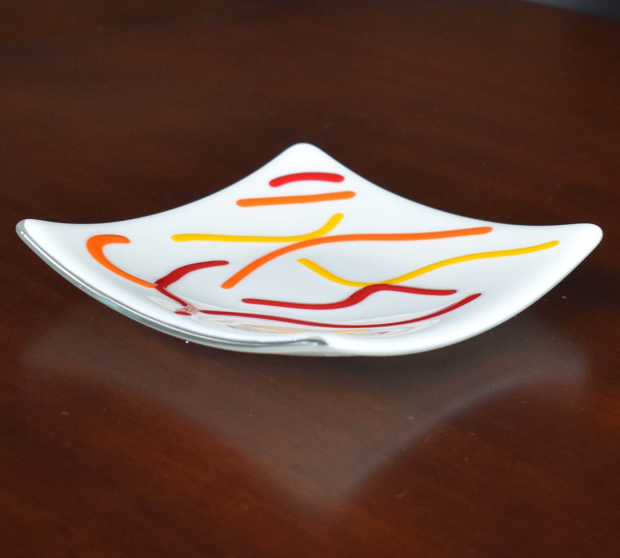 Six inch square dish in creamy white with abstract design of orange, red and yellow fused glass