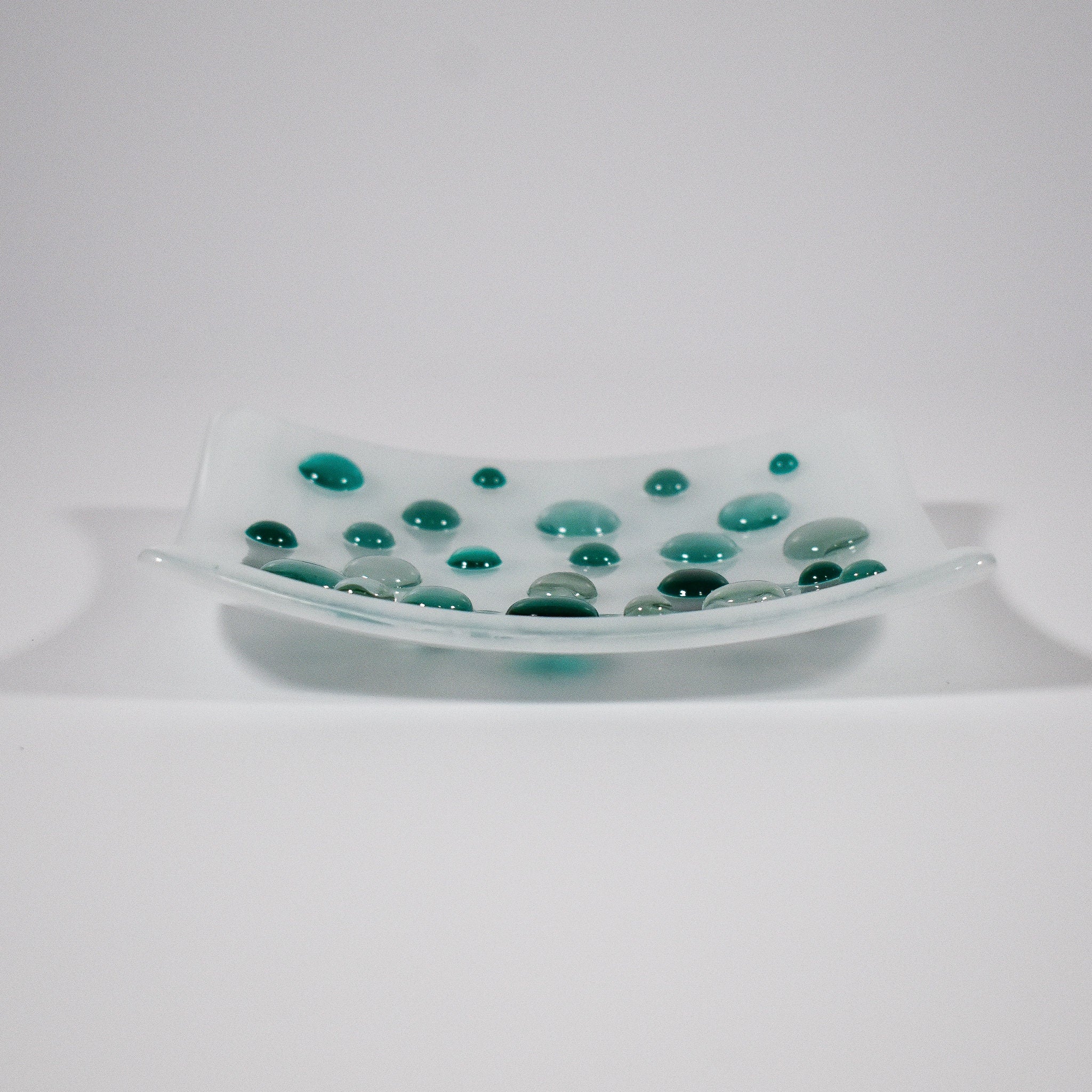 Pure white square glass dish with round glass pebblest; in various shades of teal green. Tray is 6 inch square with sloped corners.