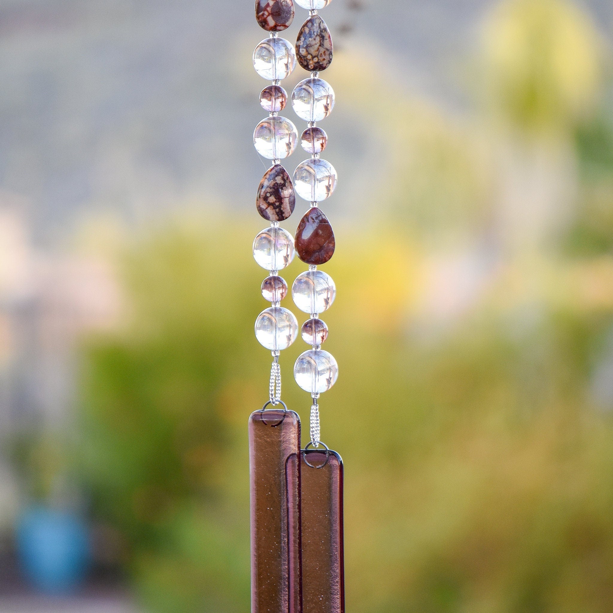 Tear-drop shaped rhyolite stones are strung with large clear glass beads and smaller pale purple beads. Anchored by two pieces of pale purple glass. Hanging from tree.