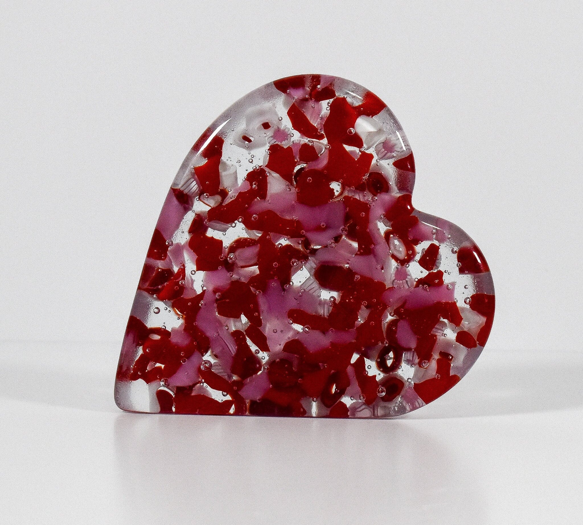 Heart-shaped solid glass paperweight standing on one side of the heart, pink and red with clear and white glass, 4-1/2&quot; tall. white background