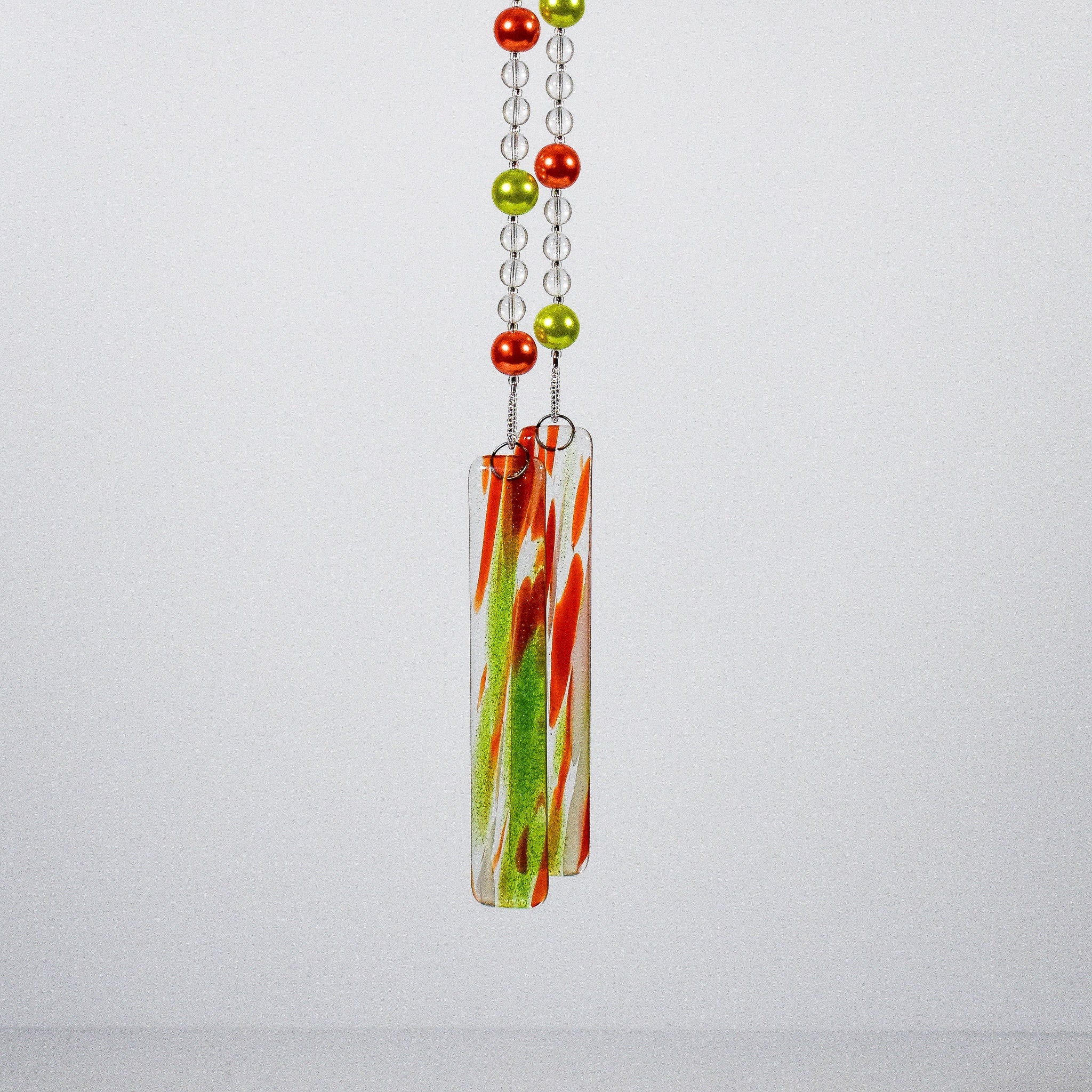 lime green and orange pearl beads hanging vertically on wire with smaller clear glass beads, against white background, anchored by two pieces of orange and green fused glass.