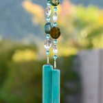 Green agate slice beads strung with glass crystal beads, hanging vertically from tree, anchored by two pieces of teal green fused glass