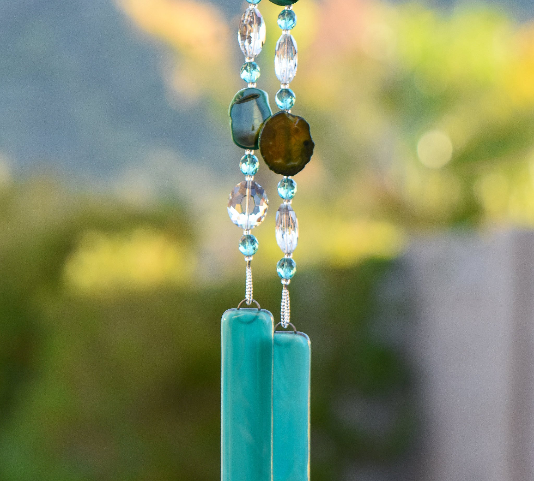 Green agate slice beads strung with glass crystal beads, hanging vertically from tree, anchored by two pieces of teal green fused glass