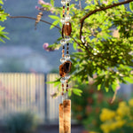 Two beaded wires hanging vertically from Vitex tree. Beads include large black agate slices, smaller agate tubular beads and large clear glass beads. Wire is anchored by two brown and white fused glass pieces.