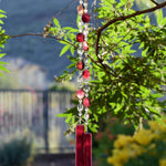 Coin-shaped pink agate slice beads strung with clear glass crystal beads, hanging vertically from a tree, anchored by two pieces of cranberry pink fused glass.