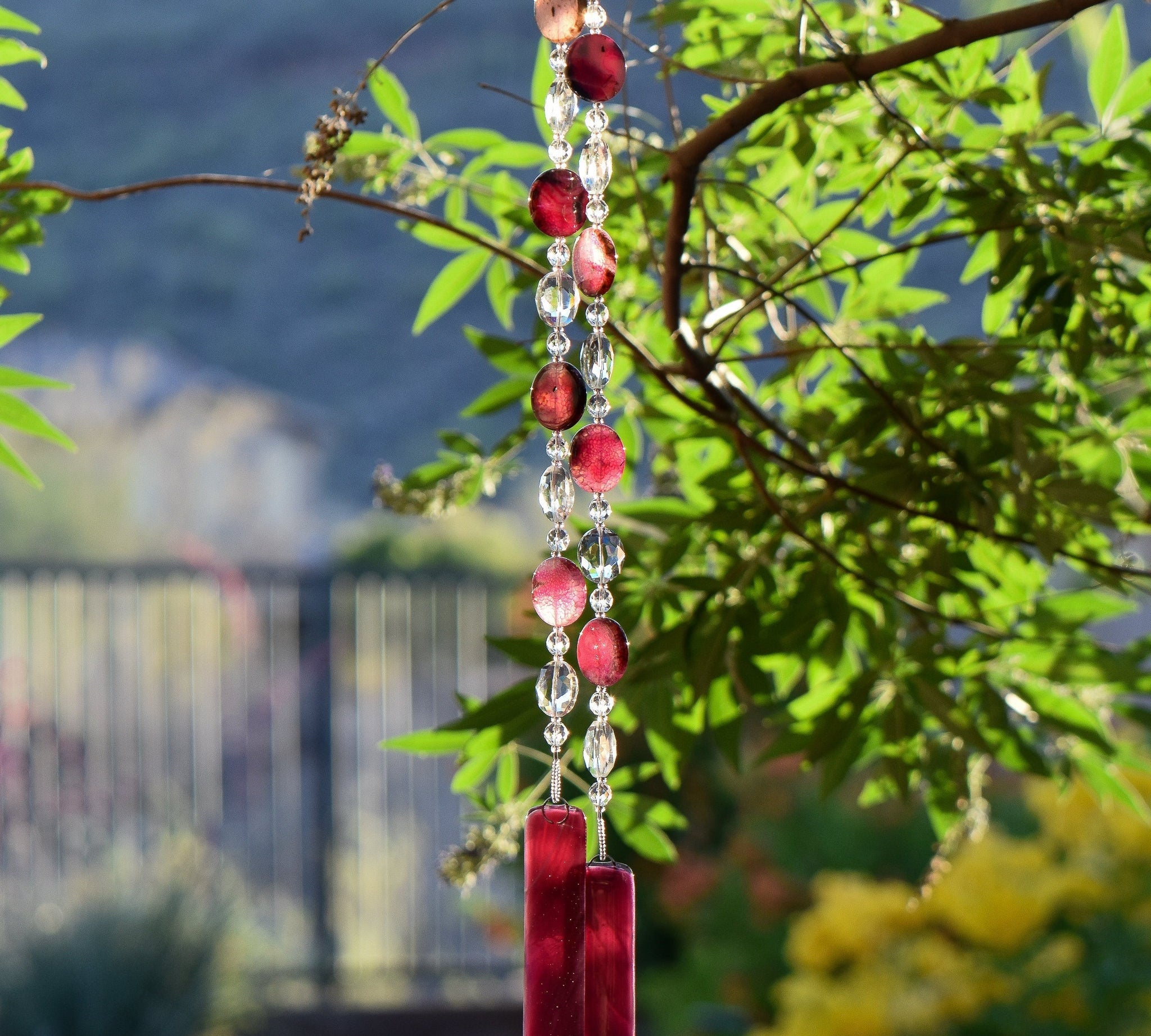 Coin-shaped pink agate slice beads strung with clear glass crystal beads, hanging vertically from a tree, anchored by two pieces of cranberry pink fused glass.