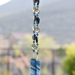 Blue agate slice beads strung with blue and silver glass beads, hanging vertically, anchored by two pieces of fused glass.