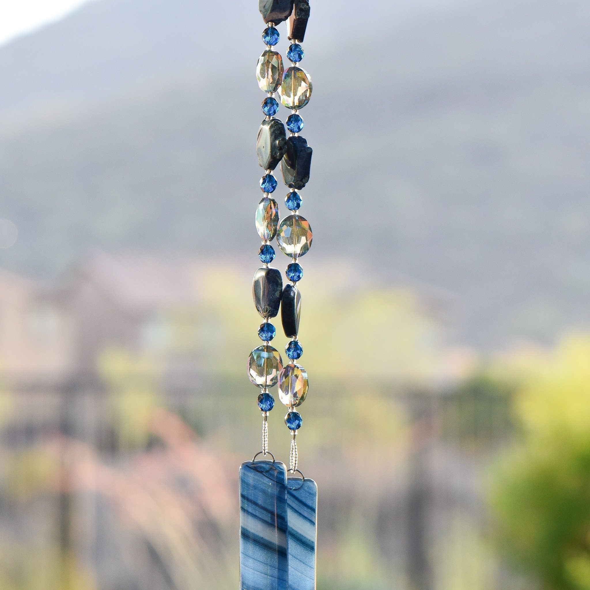 Blue agate slice beads strung with blue and silver glass beads, hanging vertically, anchored by two pieces of fused glass.