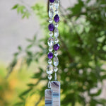 Amethyst stone beads paired with large crystal oval beads, clear glass beads, hanging vertically, anchored by two pieces of fused glass with purple/white/blue swirls.