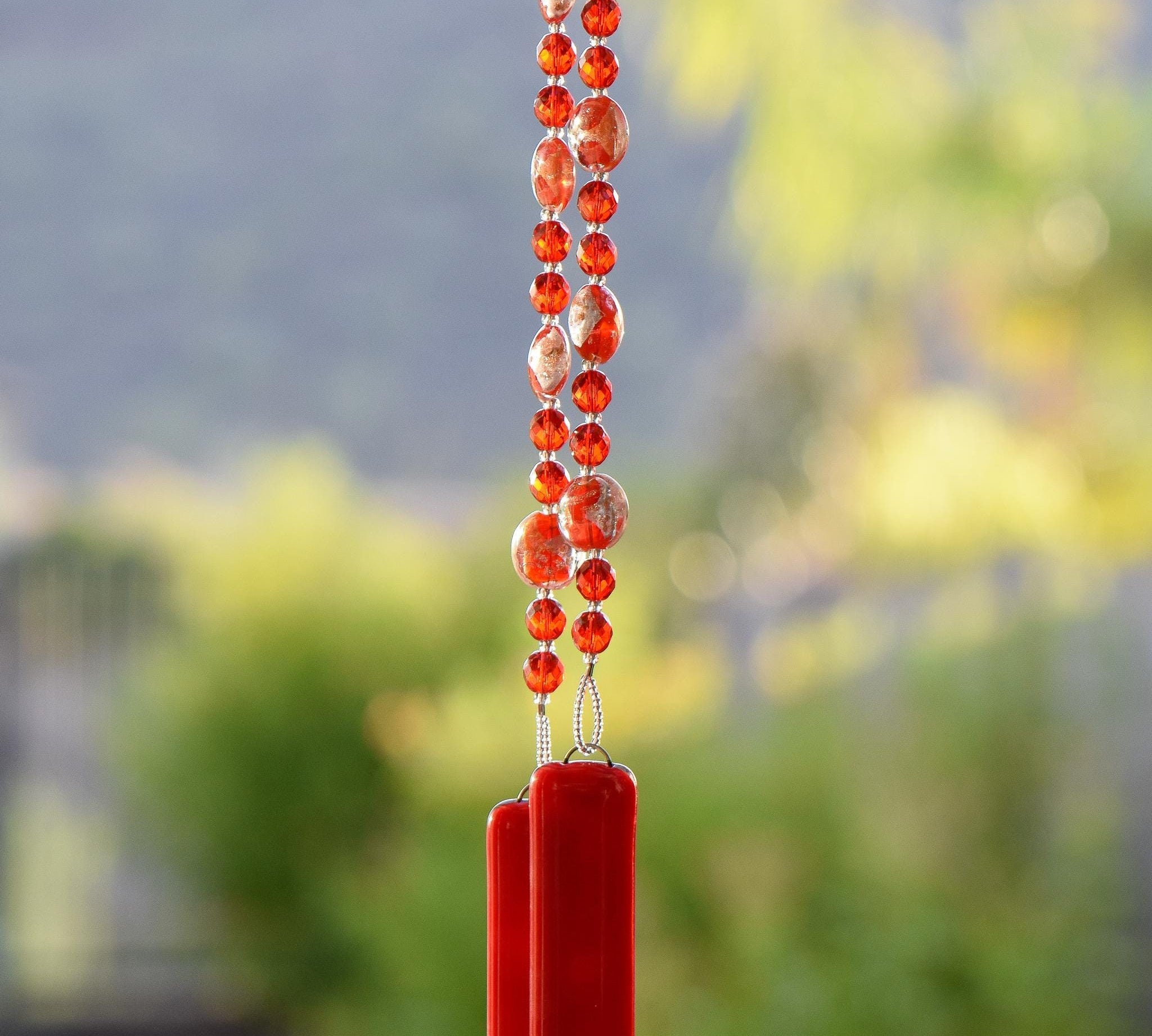 Red and gold foil lamp-worked beads are strung with solid red glass beads, hanging vertically and anchored by two pieces of opaque red fused glass.