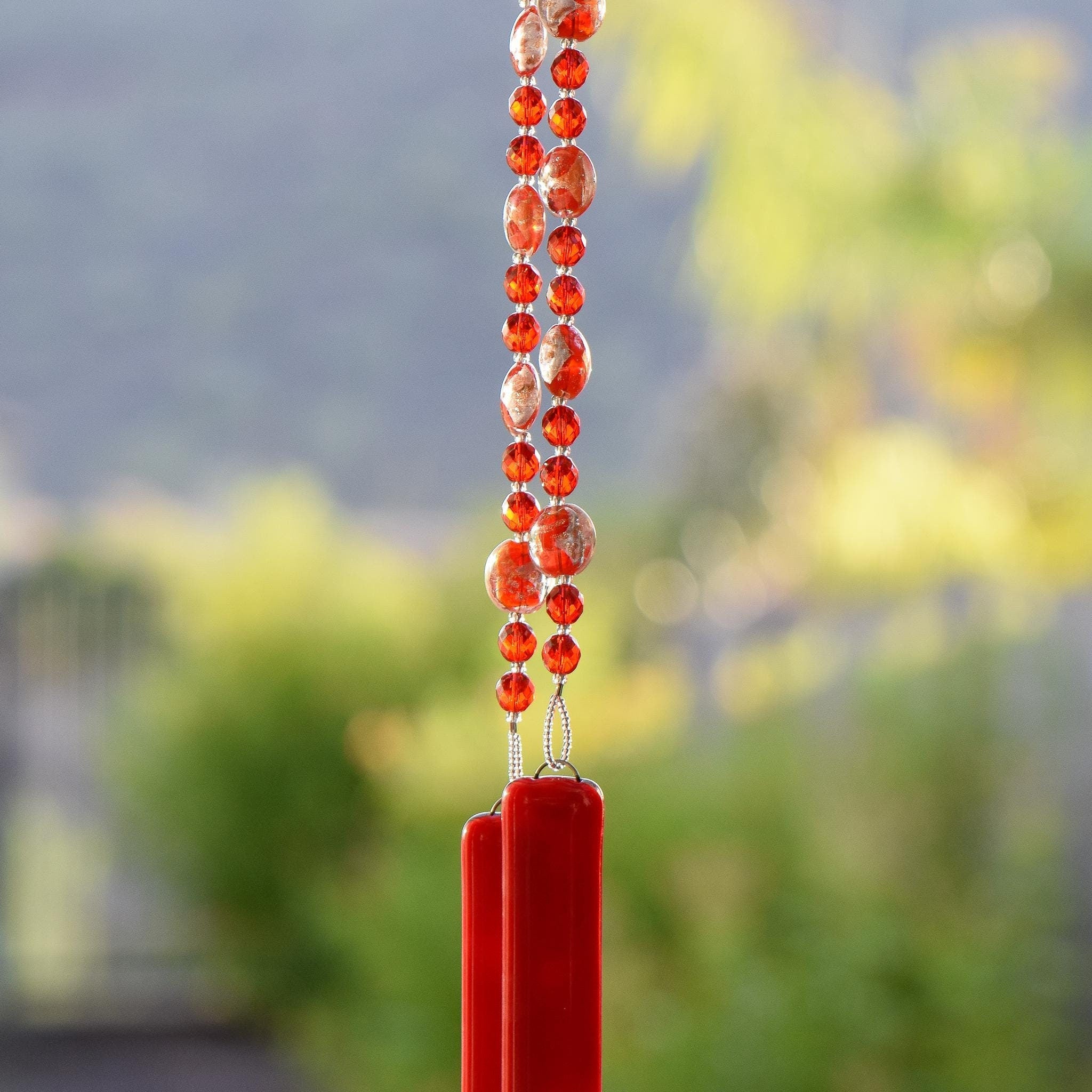 Red and gold foil lamp-worked beads are strung with solid red glass beads, hanging vertically and anchored by two pieces of opaque red fused glass.