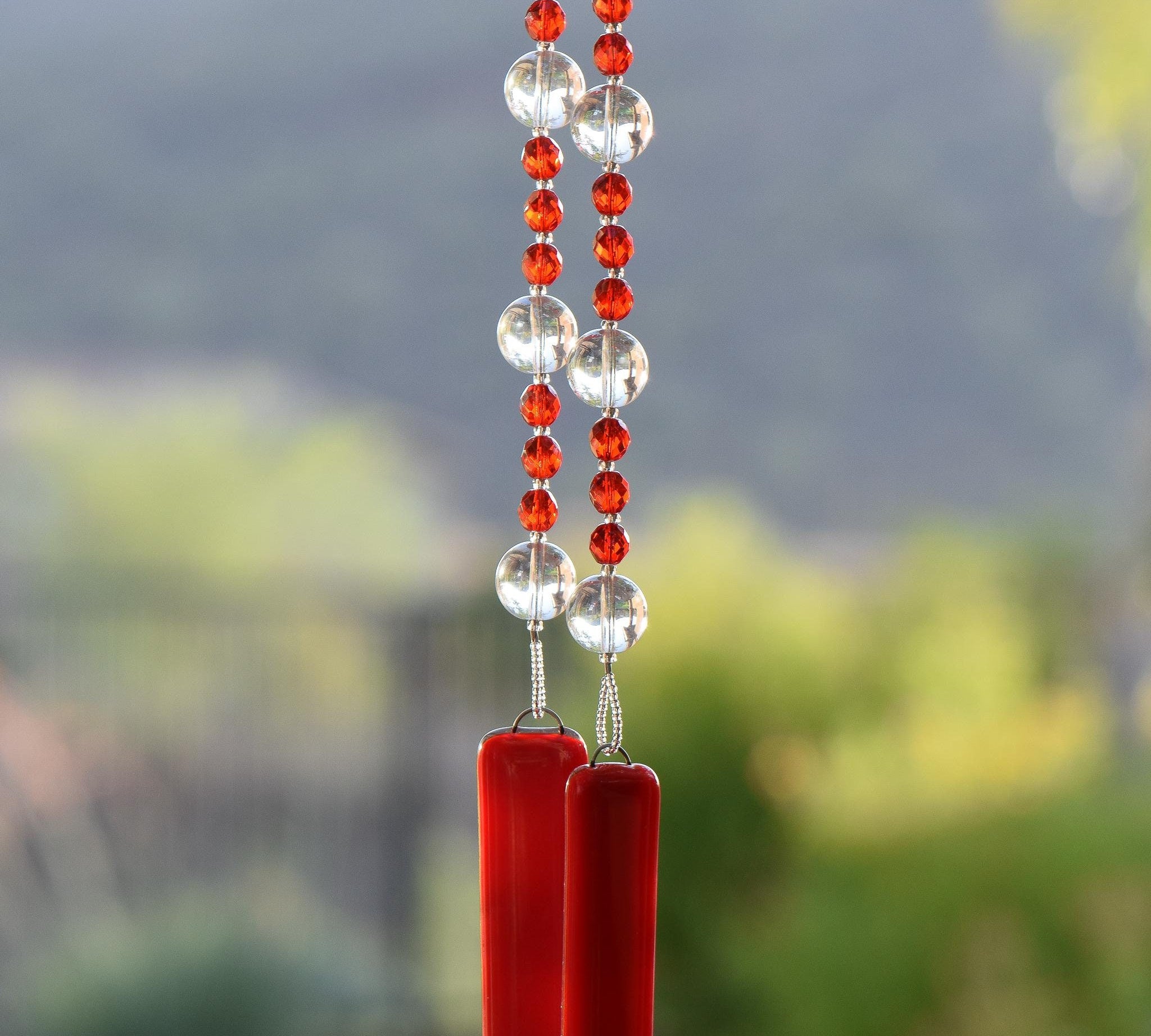 Red and clear glass beads strung together on wire, hanging vertically, anchored by two pieces of opaque red glass.