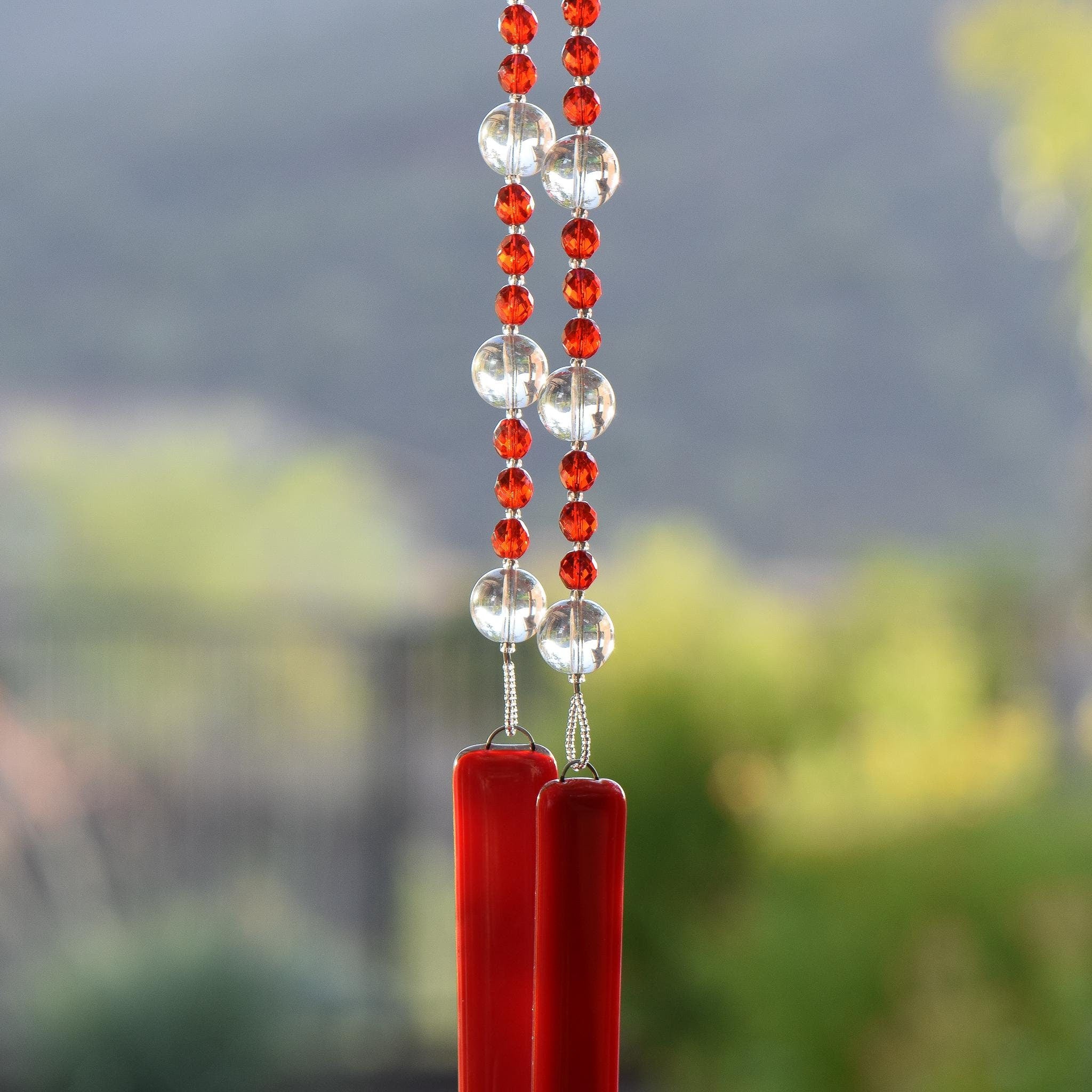 Red and clear glass beads strung together on wire, hanging vertically, anchored by two pieces of opaque red glass.