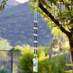 Purple pearl beads combined with large reflective glass crystal beads, strung on wire, hanging vertically, anchored by two pieces of fused glass with swirls of aqua, purple and white