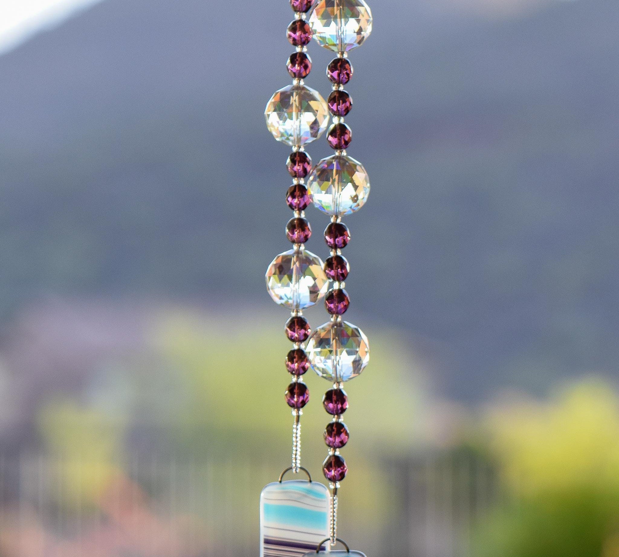 Faceted amethyst glass beads strung on wire with large glass crystal beads, hanging vertically, anchored by two pieces of kiln-formed glass