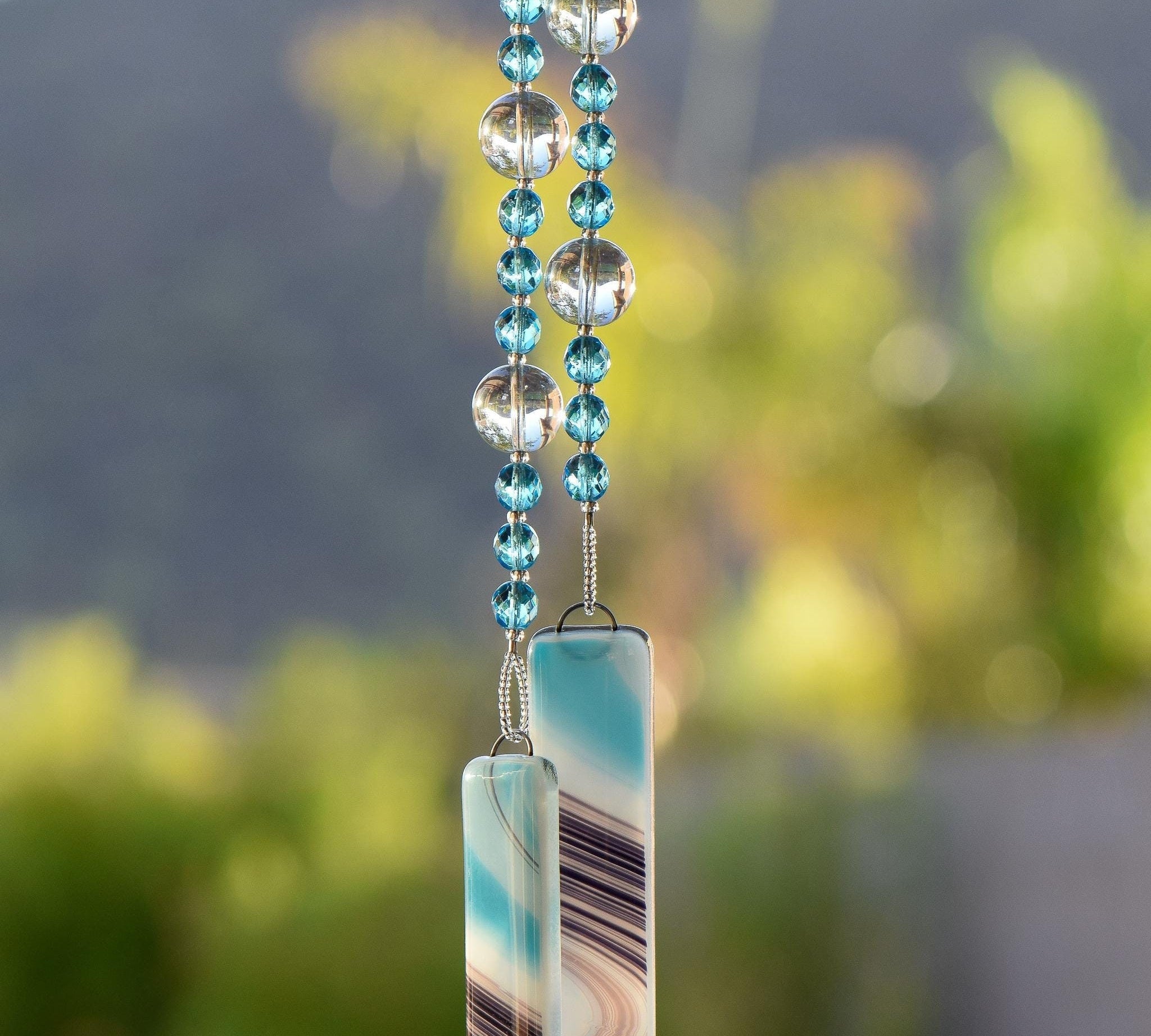 Turquoise blue faceted glass beads strung with large reflective glass, hanging, anchored by two pieces of turquoise, white and purple kiln-formed glass.