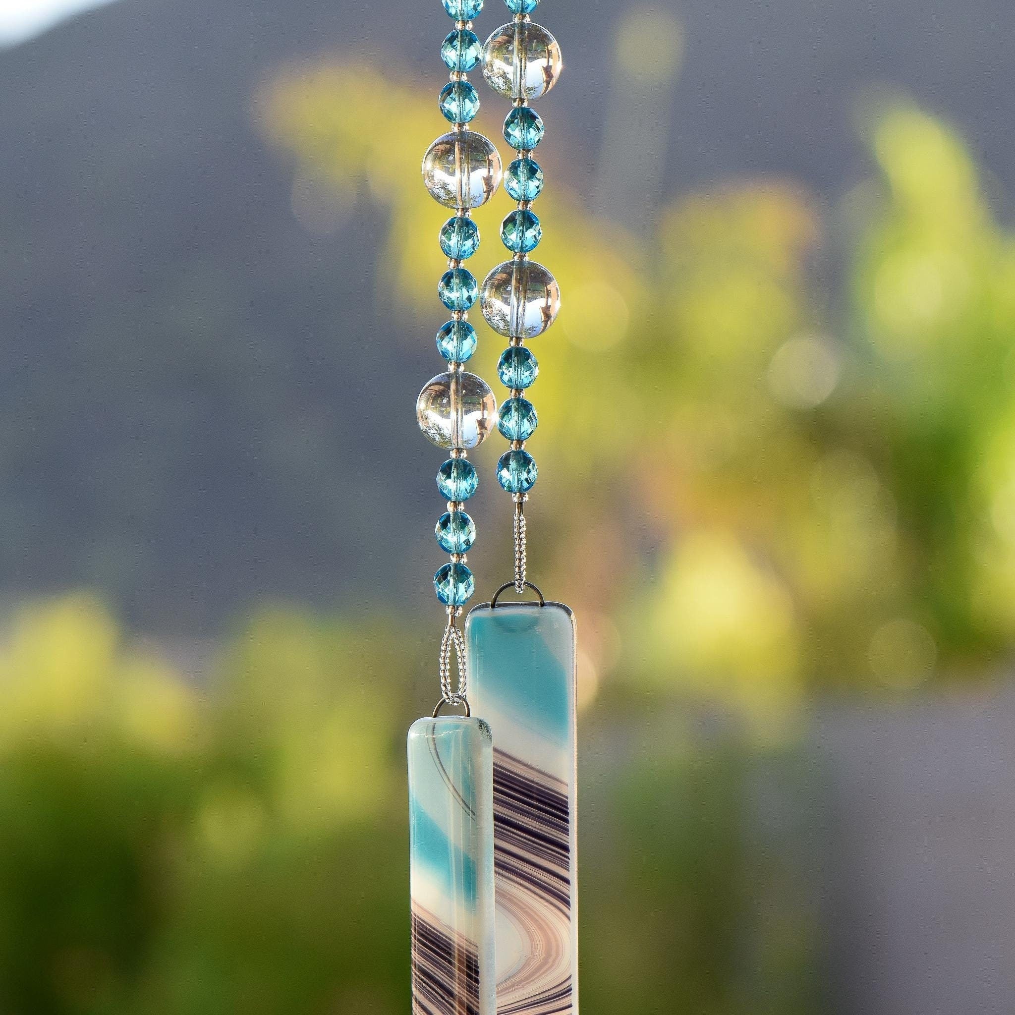 Turquoise blue faceted glass beads strung with large reflective glass, hanging, anchored by two pieces of turquoise, white and purple kiln-formed glass.