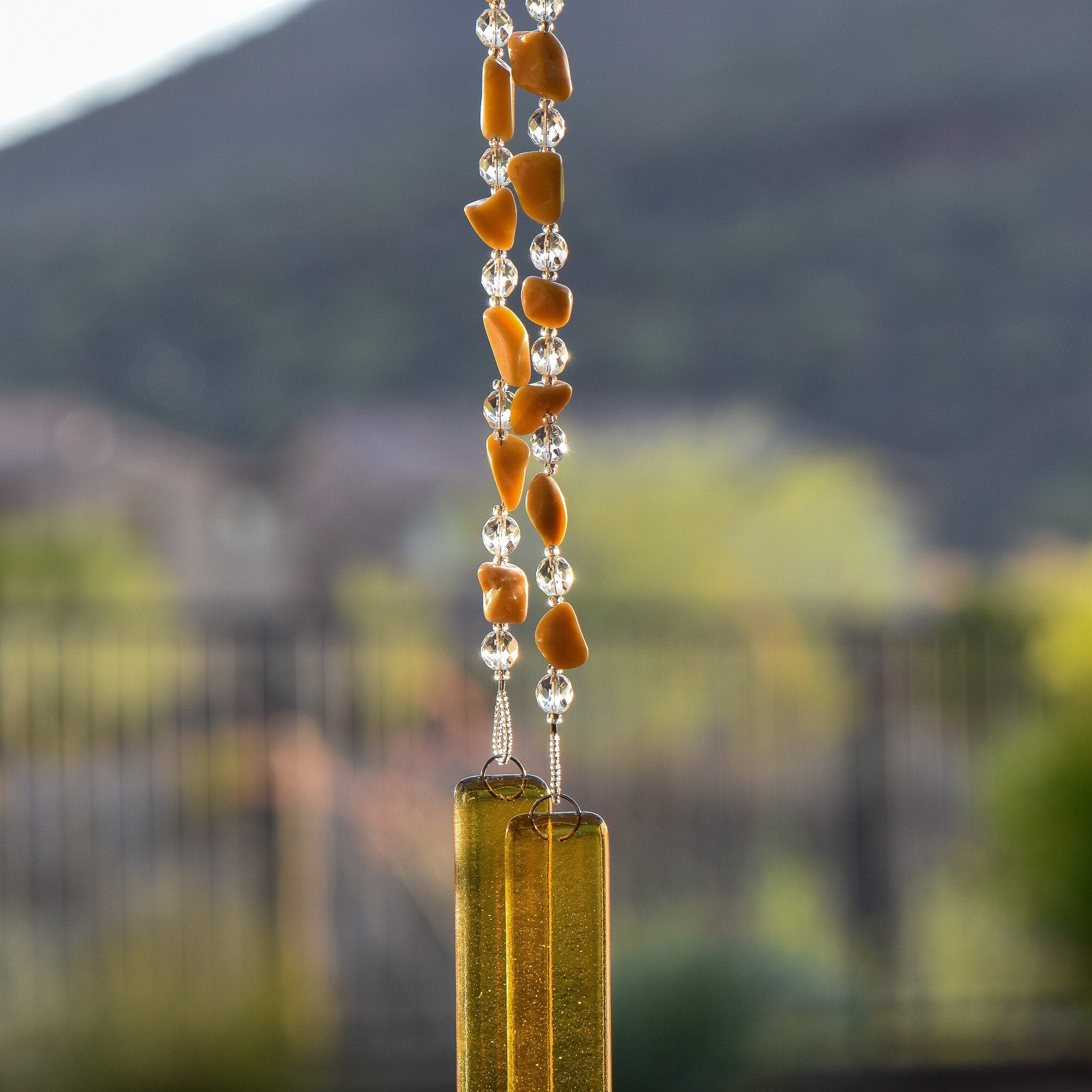 Irregularly-shaped yellow jasper stones strong with glass crystal beads and anchored by two pieces of gold fused glass, hanging vertically.