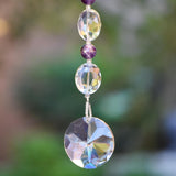 Glass crystal and amethyst stone beads strung on wire, anchored by sun-shaped crystal prism, hanging vertically from tree.