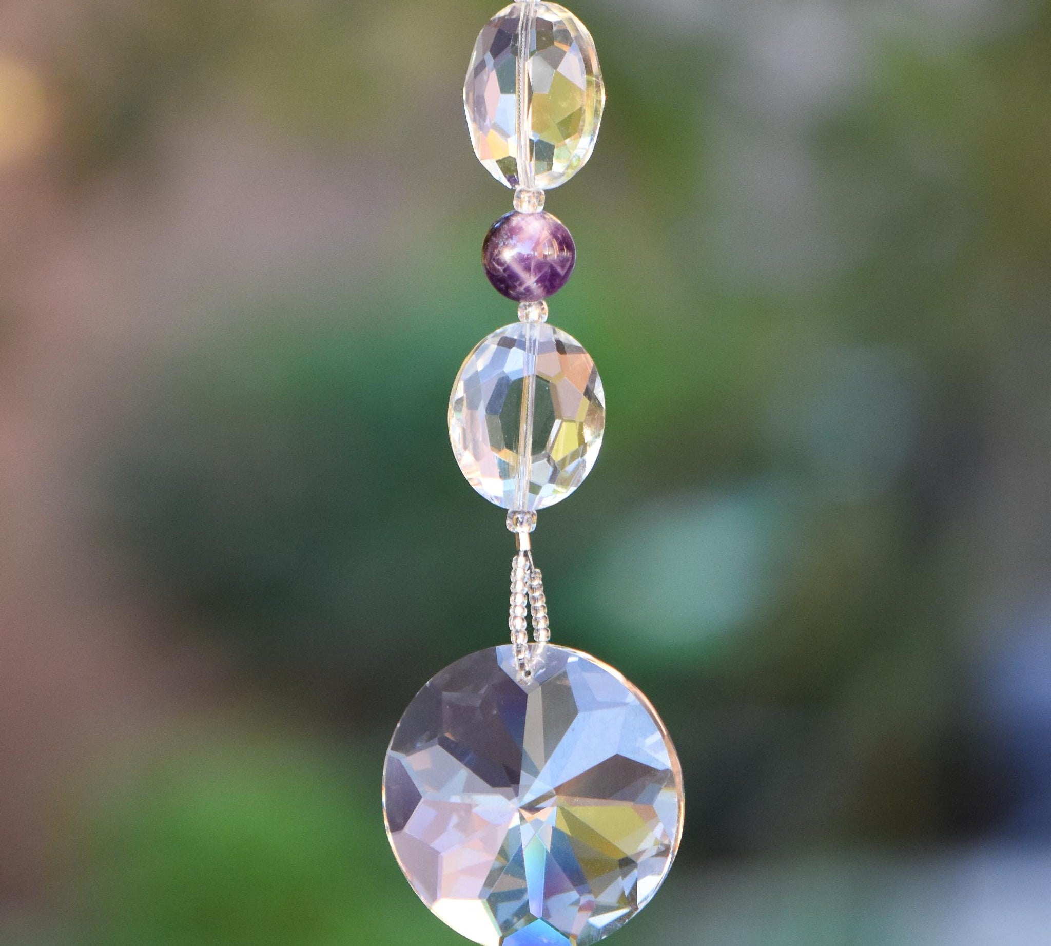 Glass crystal and amethyst stone beads strung on wire, anchored by sun-shaped crystal prism, hanging vertically from tree.