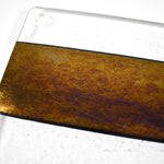 A glass cutting board with a black stripe and a gold iridescent stripe. The board has a textured surface.