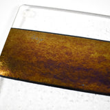 A glass cutting board with a black stripe and a gold iridescent stripe. The board has a textured surface.