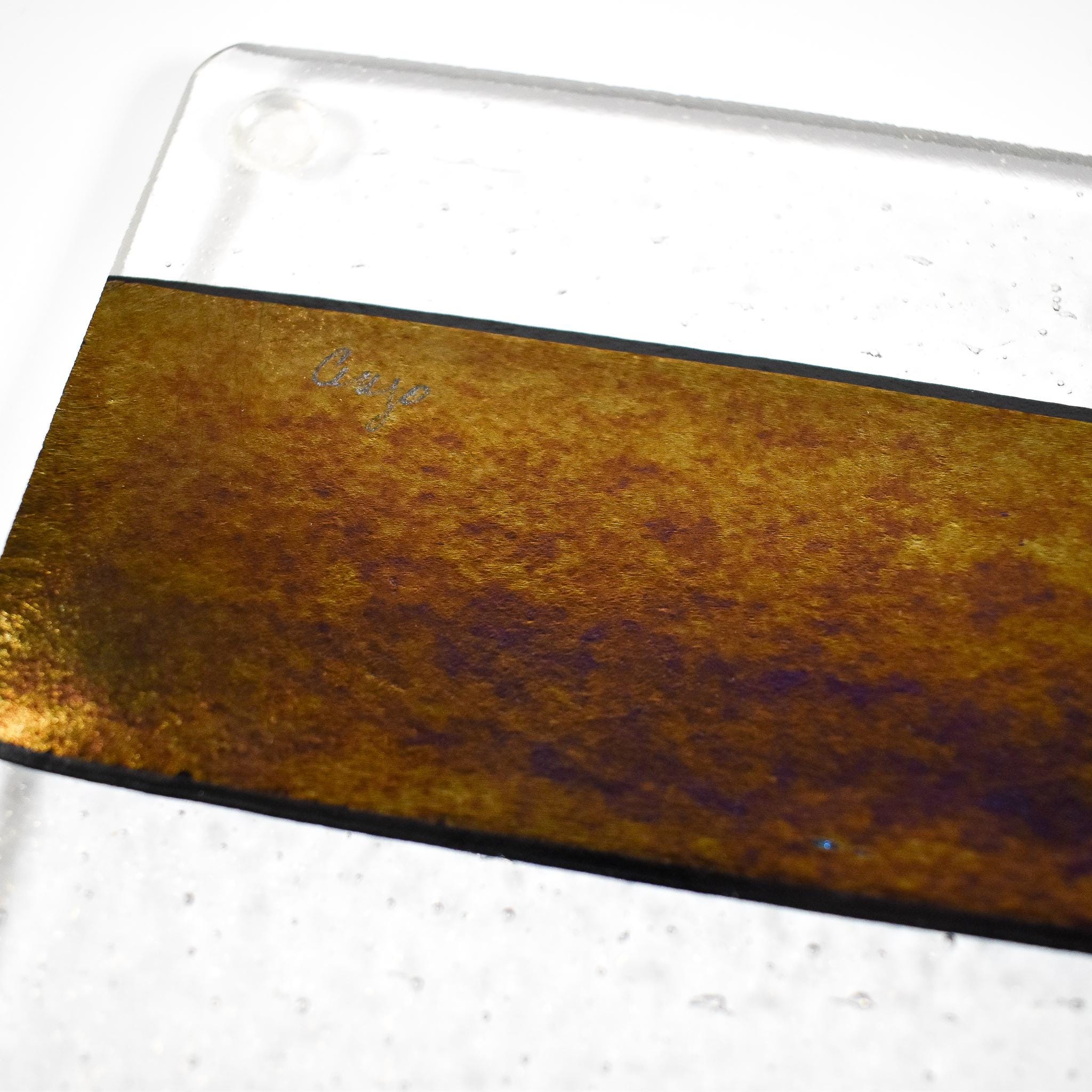 A glass cutting board with a black stripe and a gold iridescent stripe. The board has a textured surface.