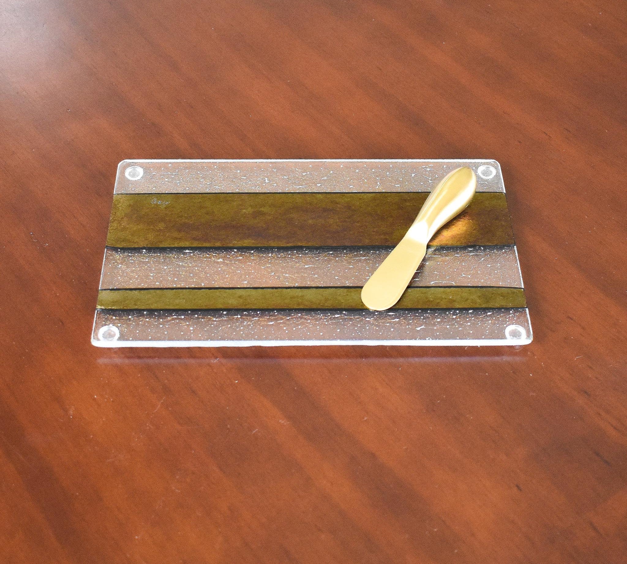 Rectangular cheese tray made with gold, black and clear iridescent fused glass. Gold spreader knife laying on top.