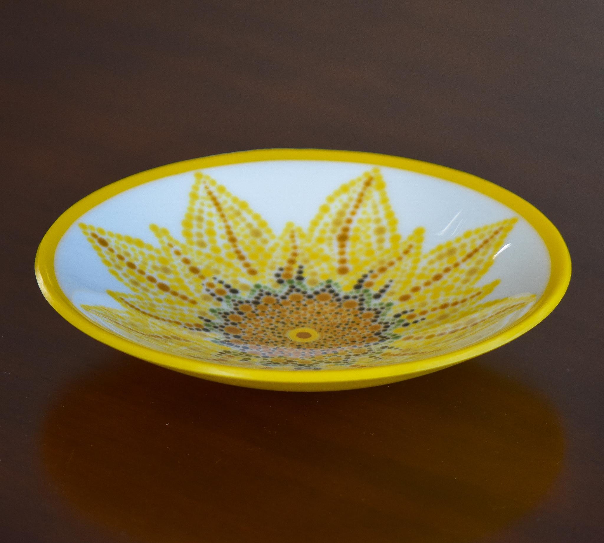 Round glass bowl with hand-painted sunflower design and bright yellow trim on wood table