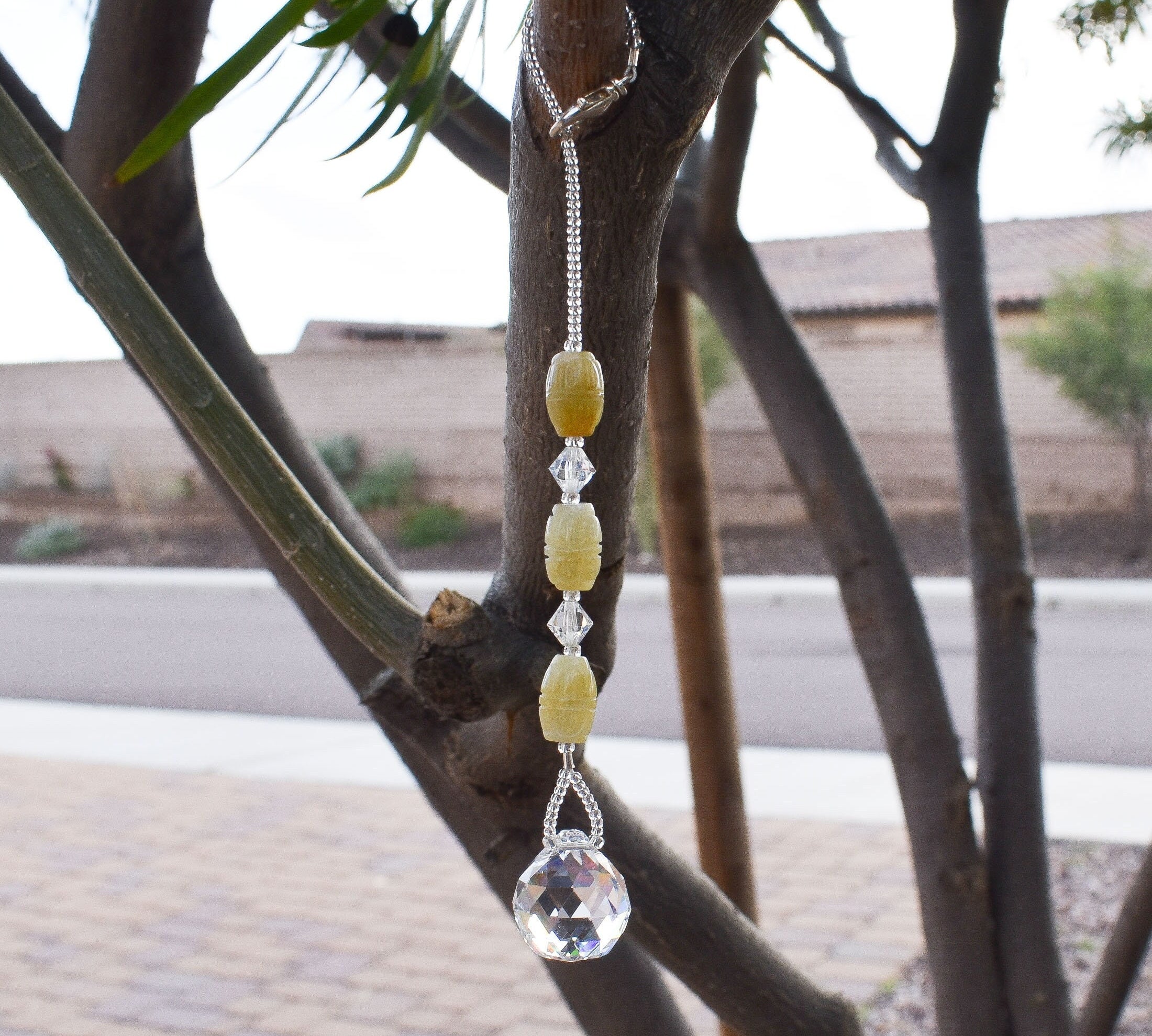 Three carved jade barrel beads flanked by crystal beads and anchored by crystal prism, hanging from tree.