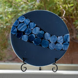 Payne&#39;s gray fused glass plate with sparkling blue accent path on stand in window